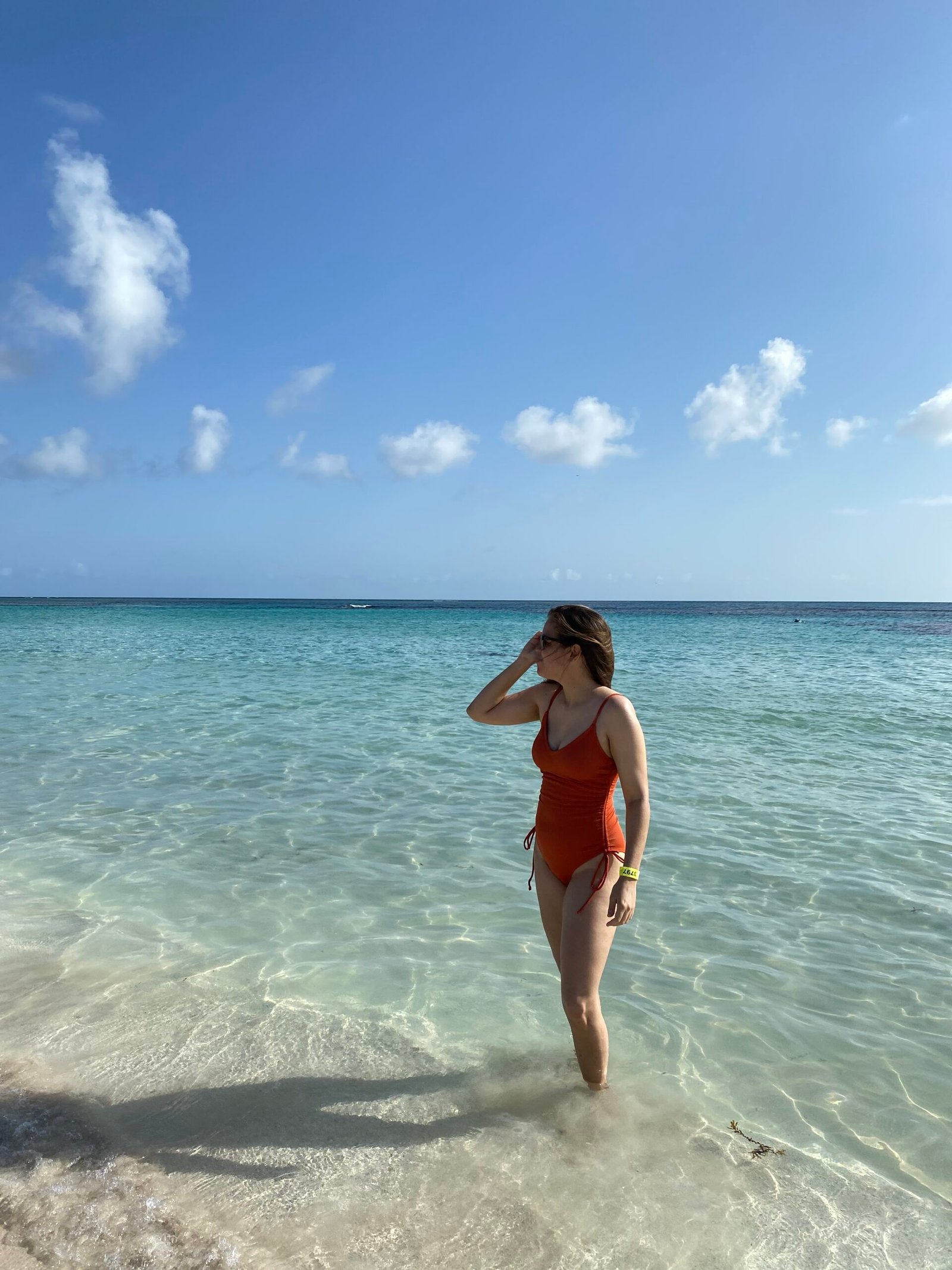 La mujer está a la orilla de la Playa Flamenco en Culebra. Viste un traje de baño completo y con un brazo sostiene sus gafas, posando para la foto.