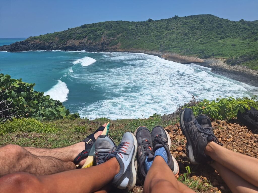 cuatro pares de piernas de cuatro amigos sentados en la parte superior de una montaña con una vista al mar