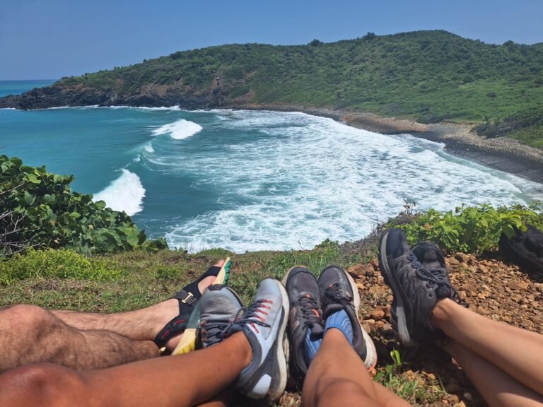cuatro pares de piernas de cuatro amigos sentados en la parte superior de una montaña con una vista al mar