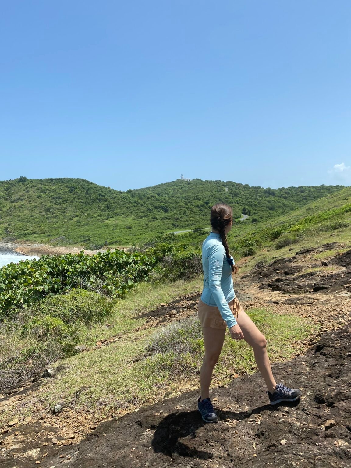 mujer está de espaldas a la cámara mirando hacia el faro de las cabezas de san juan