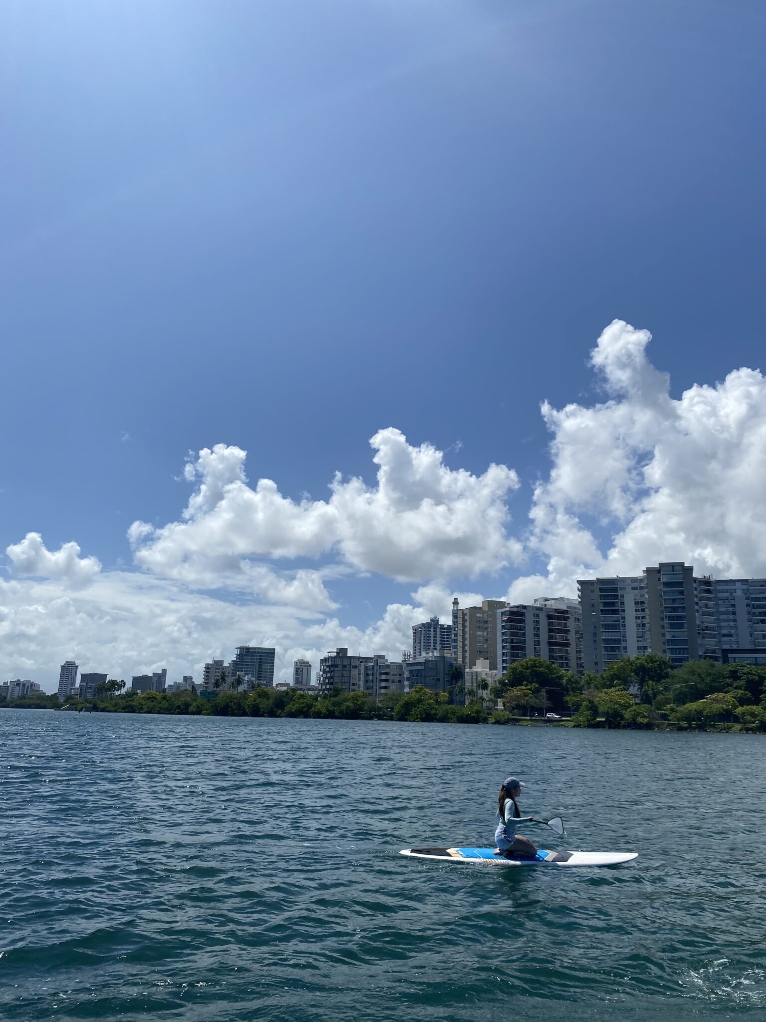 mujer haciendo paddle board de rodillas en la laguna del condado