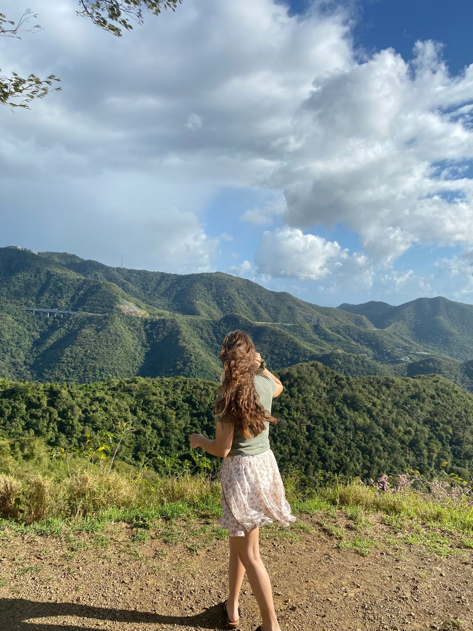 la mujer está de espalda a la cámara y de fondo está la Cordillera Central de Puerto Rico