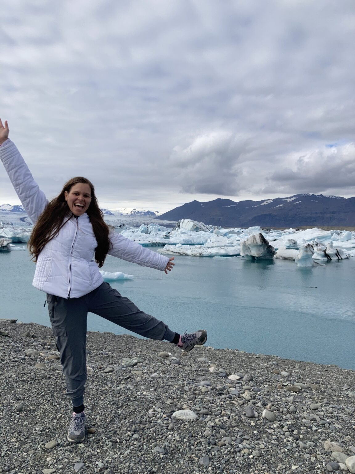 la joven esta saltando alegremente y en el fondo está la laguna con glaciares