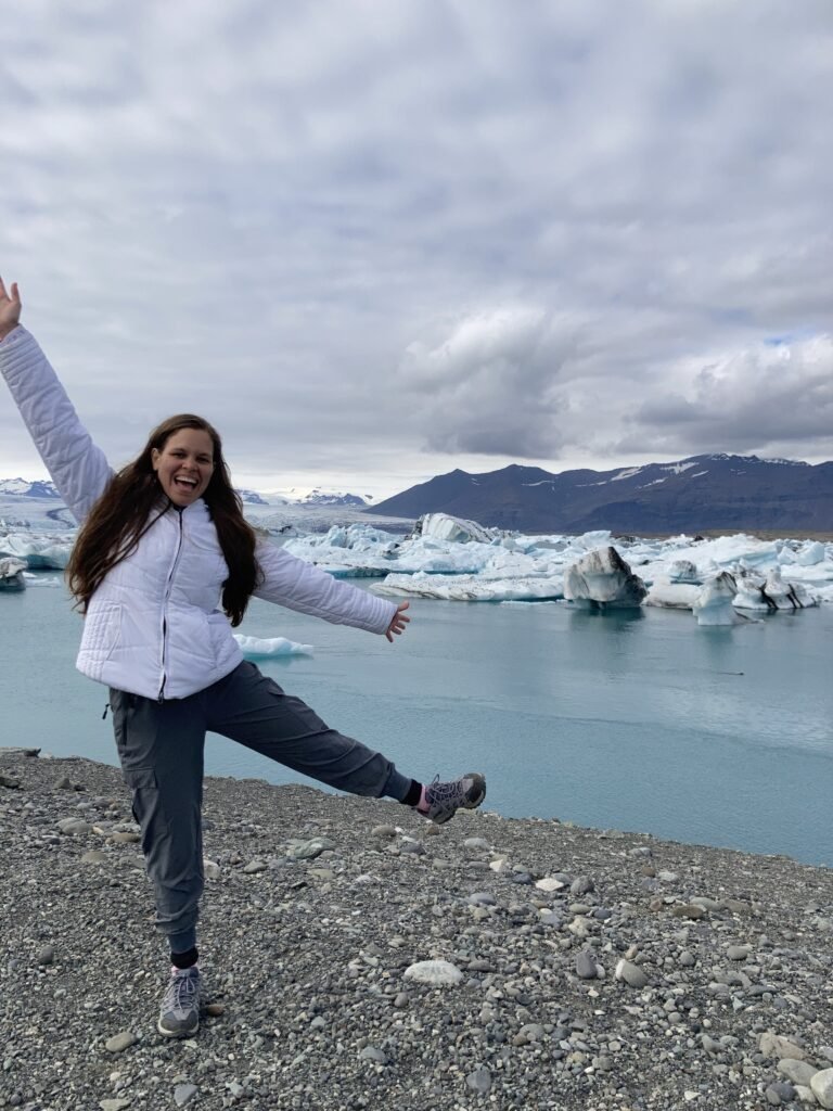 la joven esta saltando alegremente y en el fondo está la laguna con glaciares
