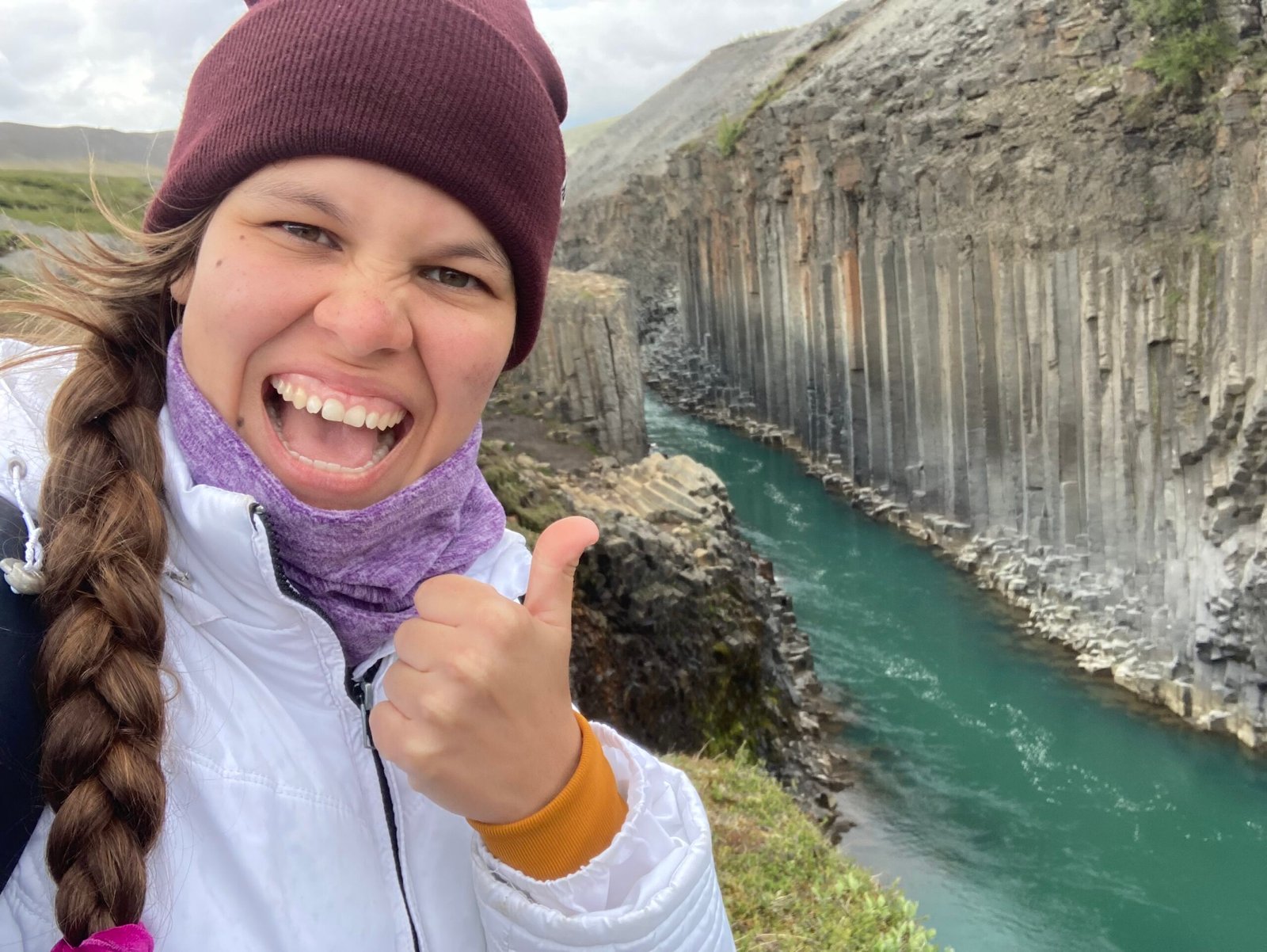 La mujer está sonriendo a la cámara y en el fondo se puede apreciar el cañón Studlagil de Islandia