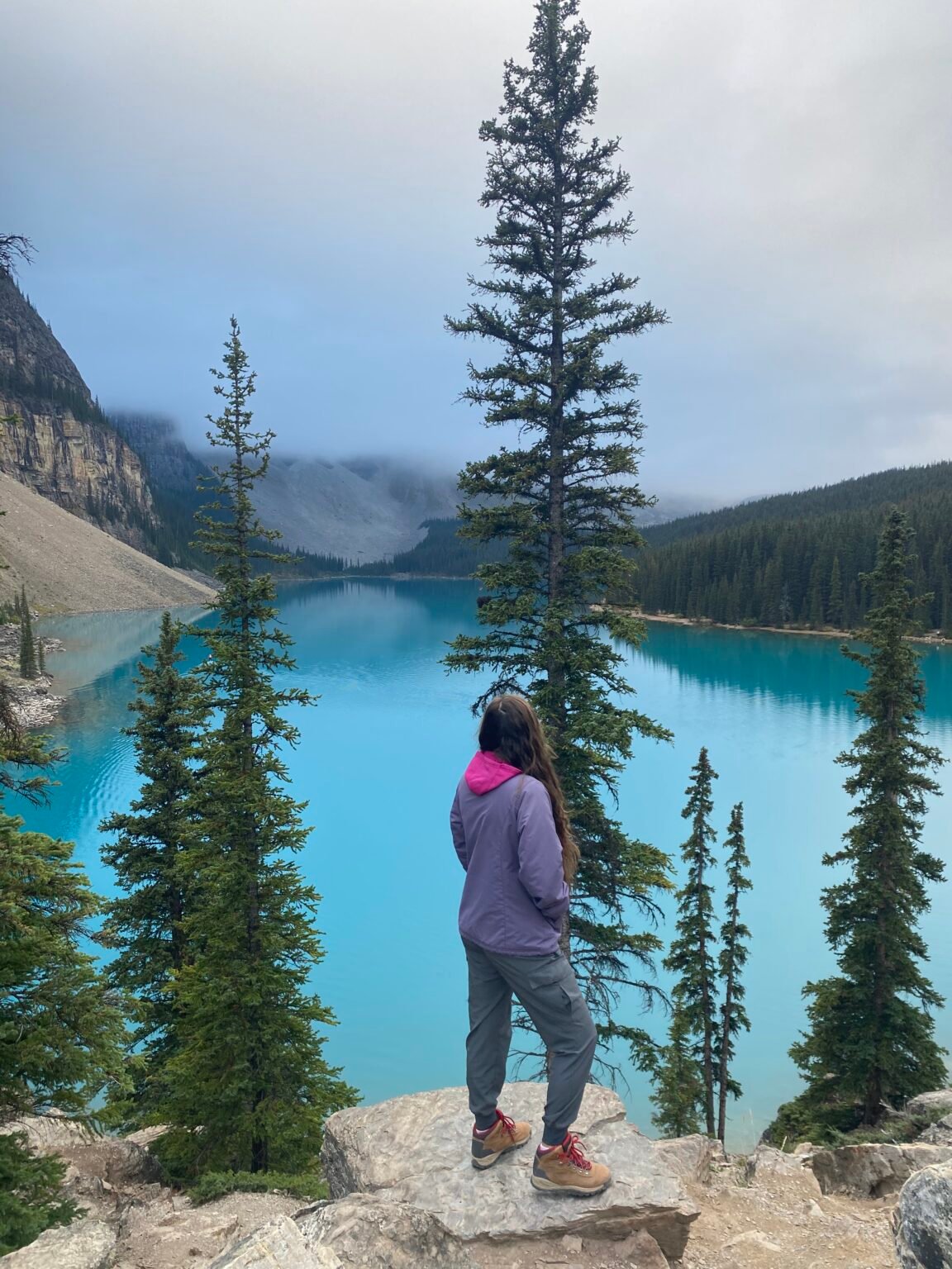 la mujer está de pie sobre una roca mirando hacia el Lago Moraine