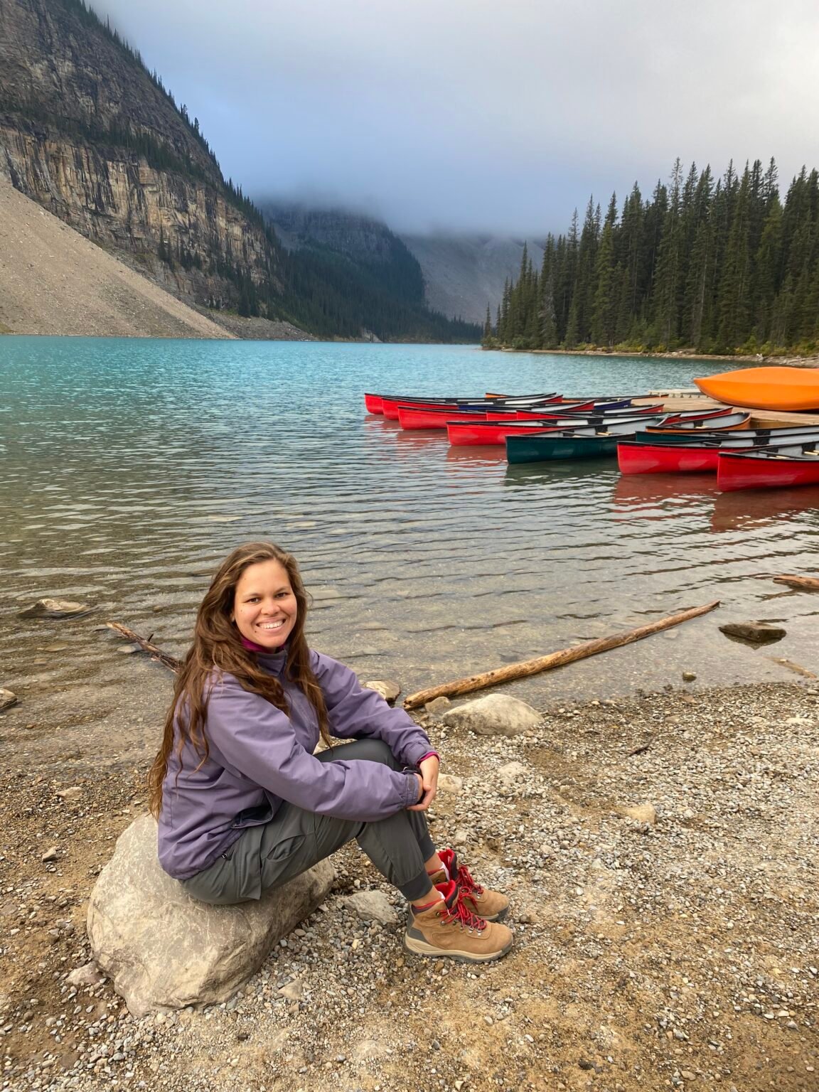 mujer sentada a orilla del lago moraine con pequeños botes de colores a su derecha