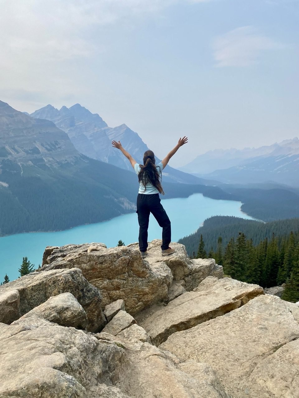 la mujer está de pie con los brazos abiertos frente a una vista del Lago Peyto en el Parque Nacional Banff, Canadá