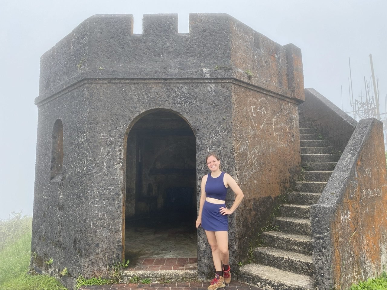 una joven posando frente a la torre de observación de pico el yunque y la neblina a su alrededor