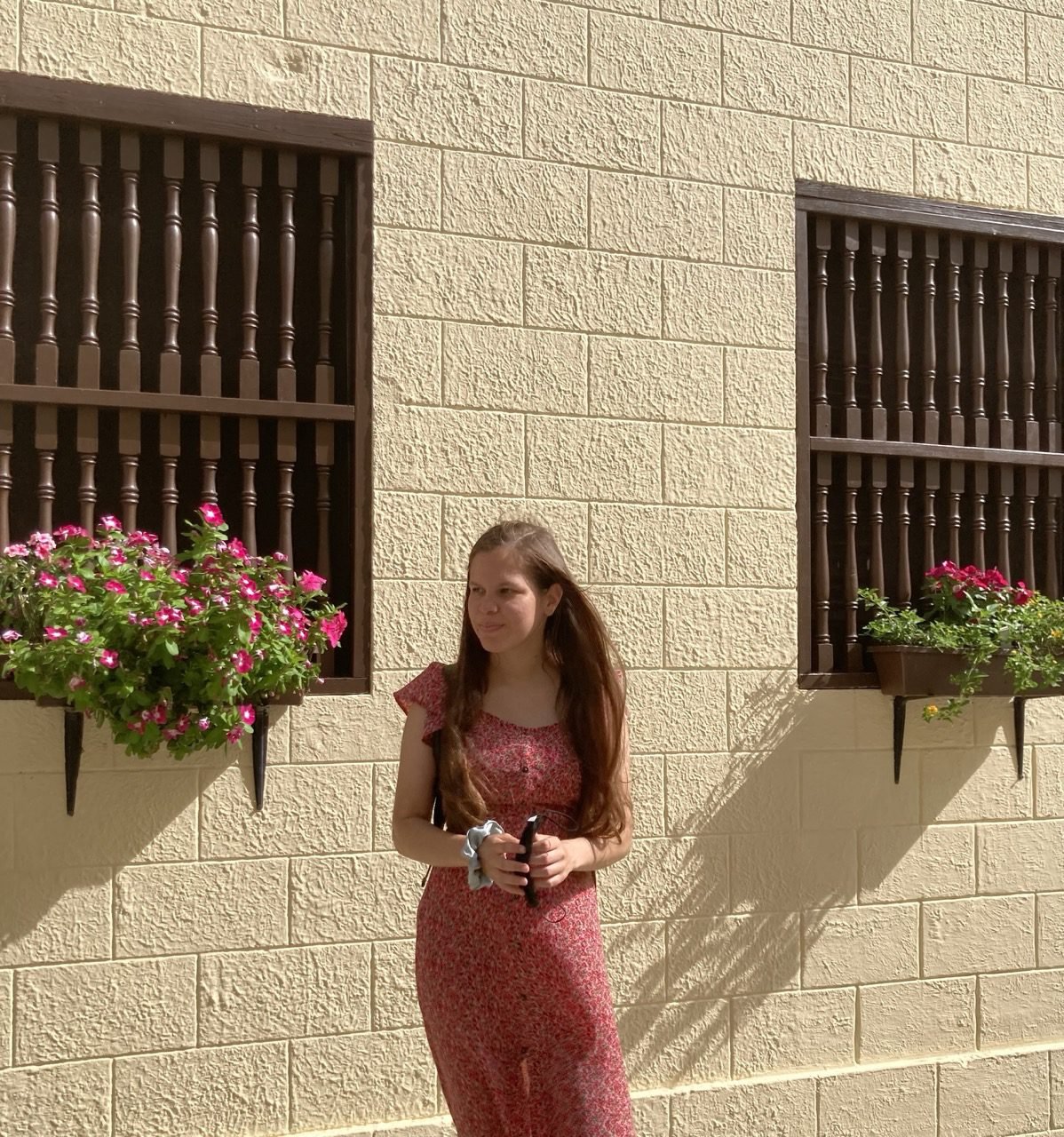 la joven viste un traje color rosa frente a una casa en el Viejo San Juan. En sus ventanas hay unos pequeños tiestos con flores color rosa.