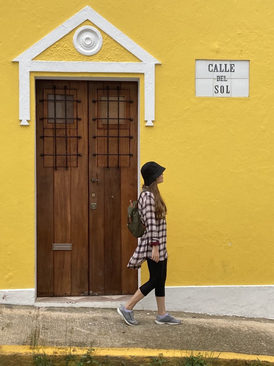 la mujer está caminando por la Calle Sol y de fondo hay una típica casa del Viejo San Juan de color amarillo